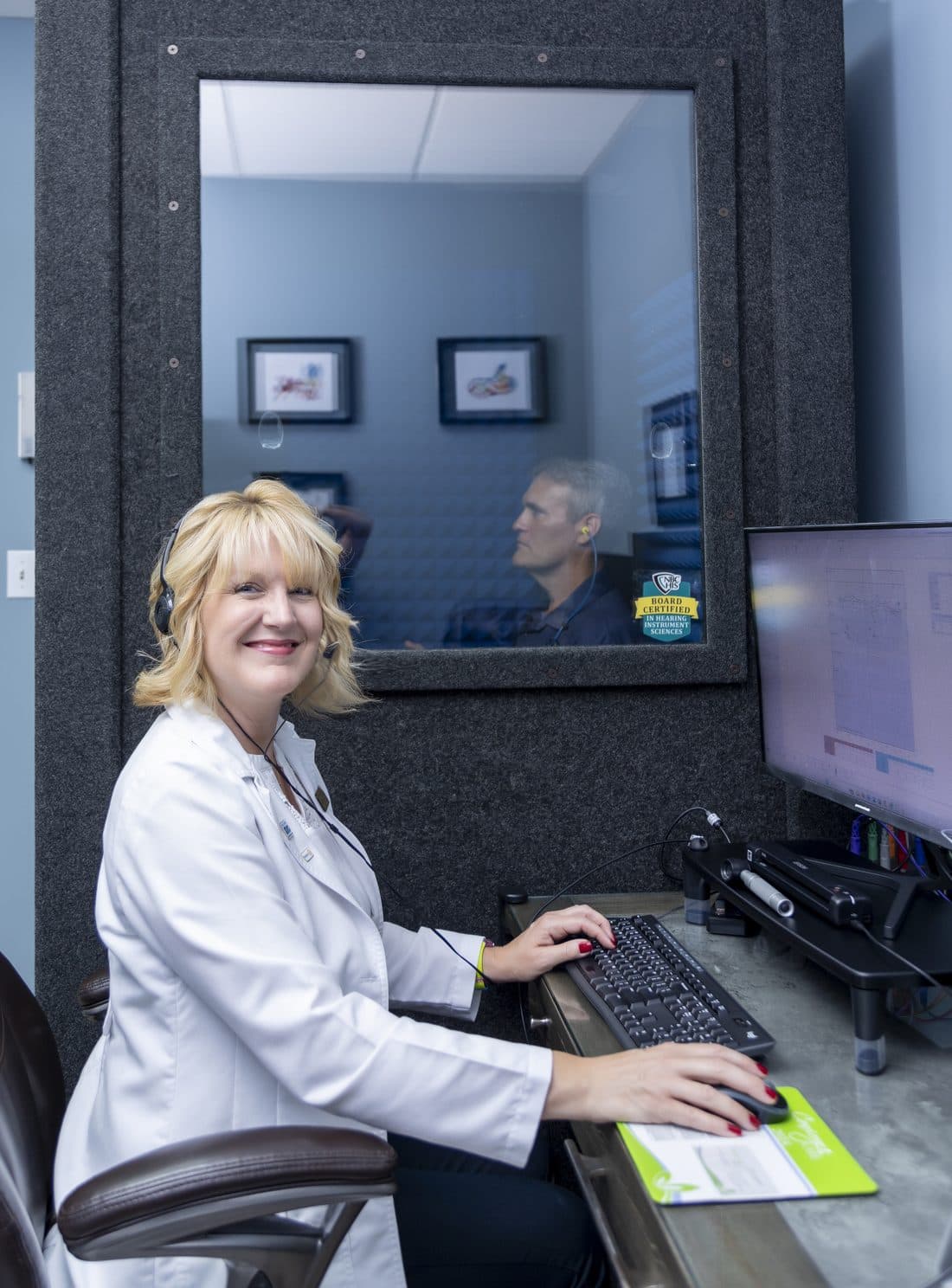 Michelle at the audiometer while a patient sits in the sound booth