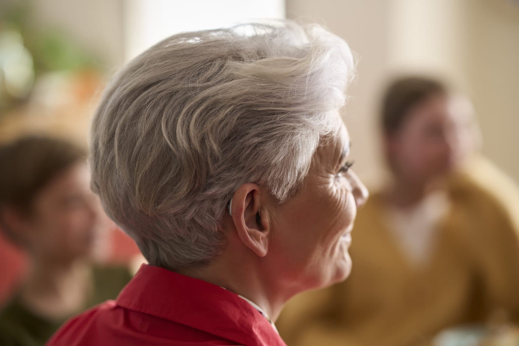 An older woman with silver hair smiling at friends in a warm room